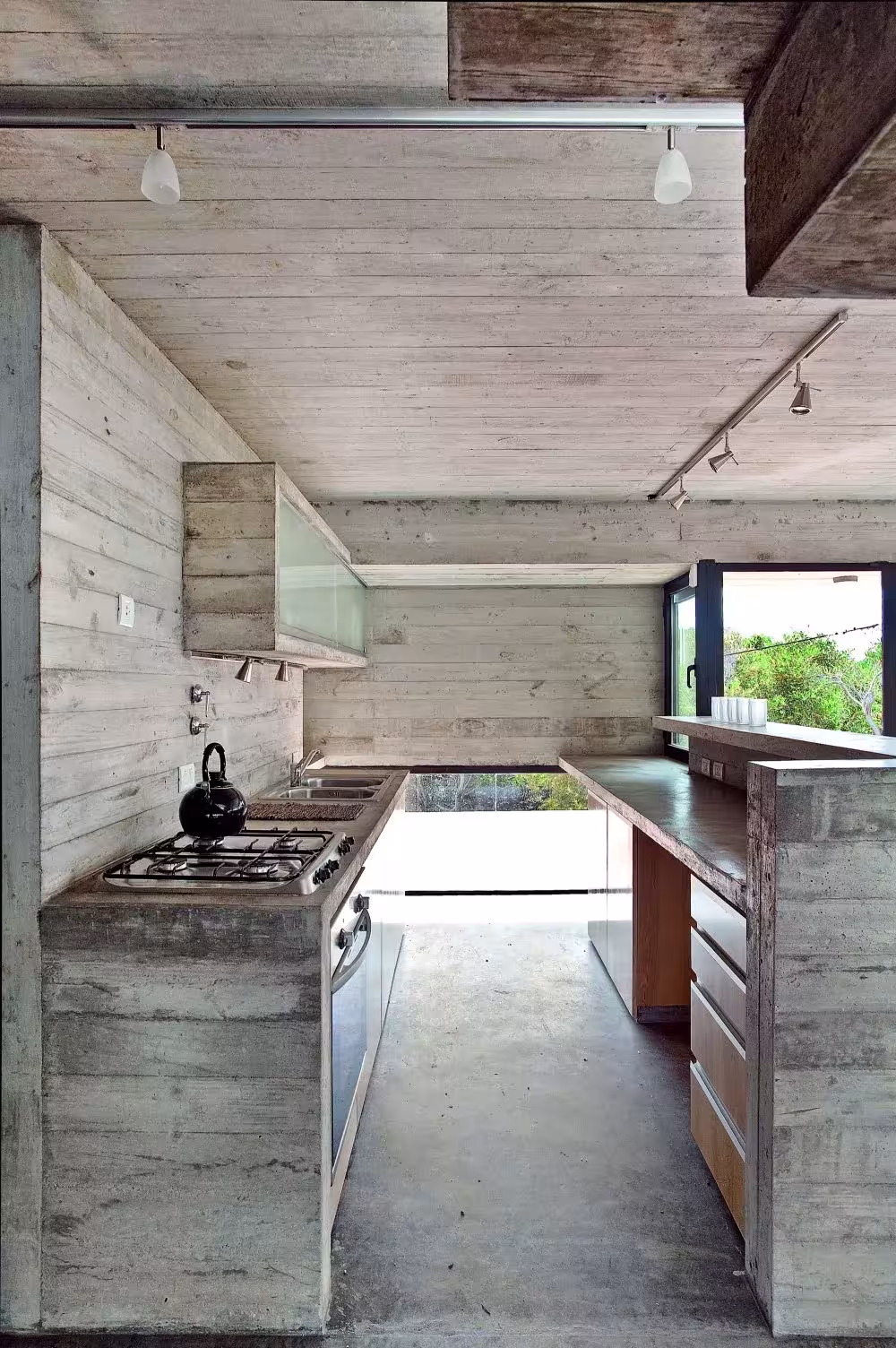 Cocina de hormigón visto con frentes de madera y fogones en la Casa en la Playa de BAK Arquitectos