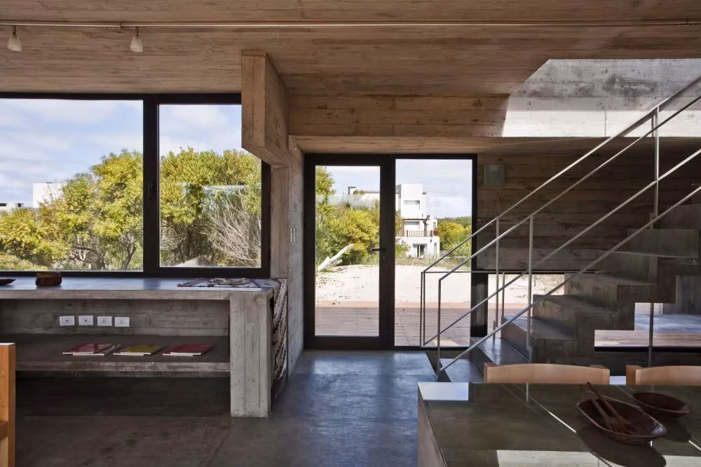 Estar de la Casa en la Playa de BAK Arquitectos con banco corrido de hormigón y escalera metálica