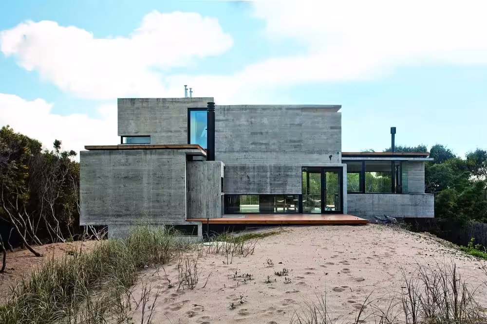 Vista frontal de la Casa en la Playa de BAK Arquitectos sobre la duna, con dos plantas de hormigón