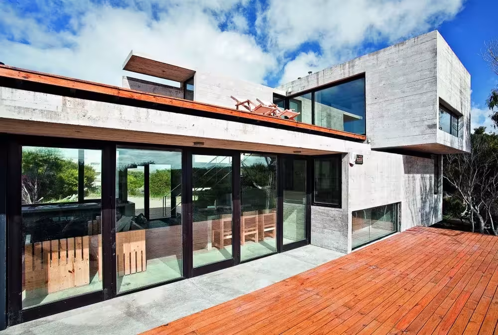 Terraza de madera junto a la fachada acristalada de la Casa en la Playa de BAK Arquitectos