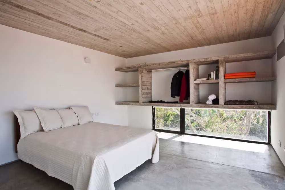 Dormitorio blanco con cama de matrimonio, estantería de madera y ventana baja en la Casa en la Playa