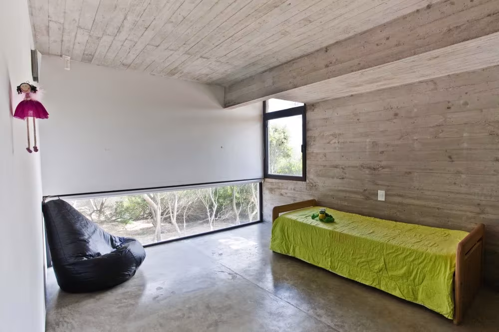 Dormitorio infantil con cama verde, puf negro y ventana alargada a ras de suelo en la Casa en la Playa