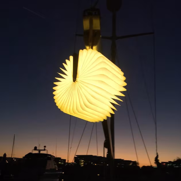 Lámpara Lumio encendida colgada de la jarcia de un velero al atardecer