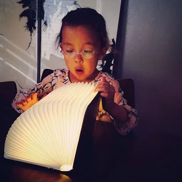 Niña con gafas abriendo sorprendida una lámpara-libro Lumio encendida