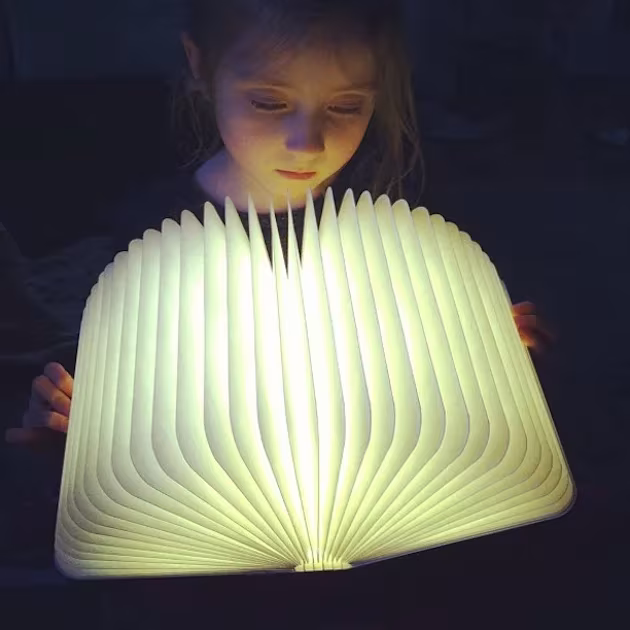 Niña iluminada por la luz de una lámpara Lumio abierta como un libro en la penumbra