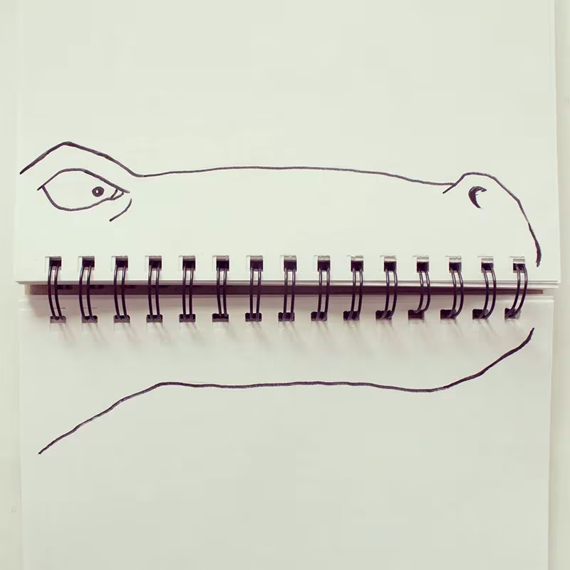 Cuaderno de espiral convertido en las fauces de un cocodrilo dibujado con tinta negra