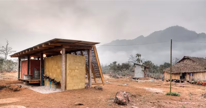 Casa de baños del orfanato Safe Haven de TYIN Tegnestue, con cubierta de madera sobre tierra rojiza en Tailandia