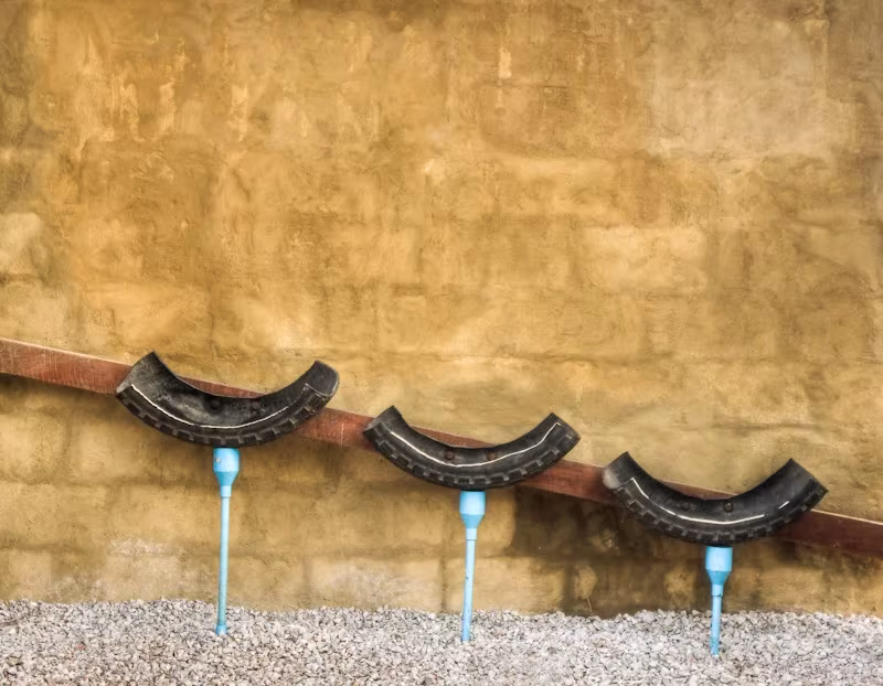 Lavabos hechos con neumáticos cortados y grifos azules sobre un muro de tierra ocre