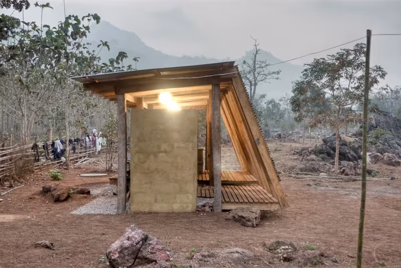Lateral inclinado de la casa de baños de TYIN Tegnestue con luz interior y montañas en la niebla