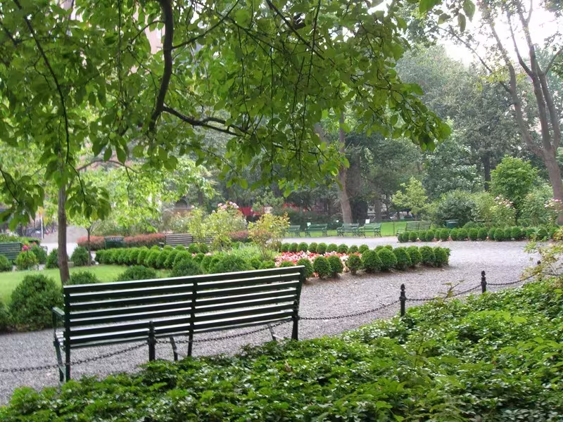 Banco verde de hierro junto a un camino de grava y setos en Gramercy Park, Manhattan