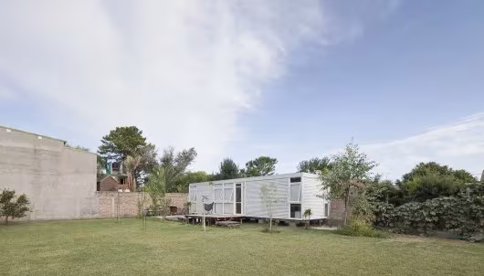 Mia House a lo lejos en un jardín amplio de césped junto a una medianera de hormigón