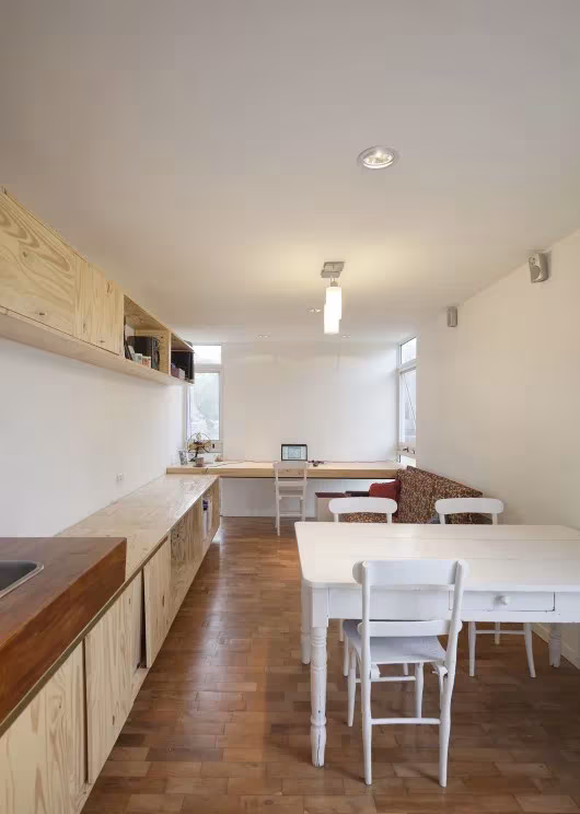 Interior alargado de la Mia House con mesa blanca, sillas y encimera de madera bajo la ventana