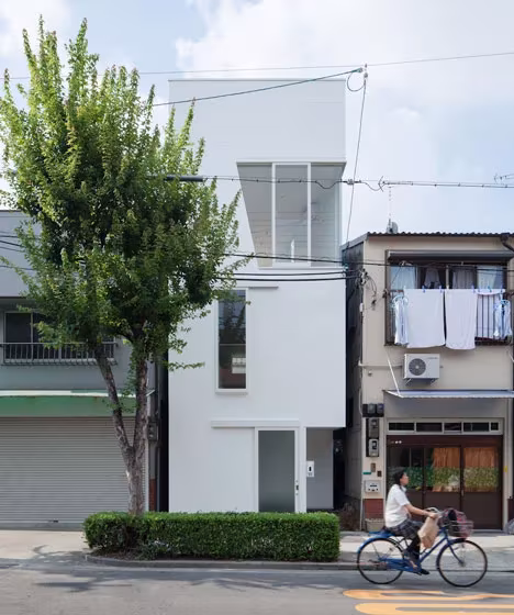 Fachada blanca de la Casa Tamatsu de Ido, Kenji en una calle de Osaka, con un árbol y una ciclista