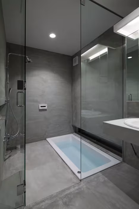 Baño de hormigón gris con bañera empotrada en el suelo y mamparas de vidrio en la Casa Tamatsu