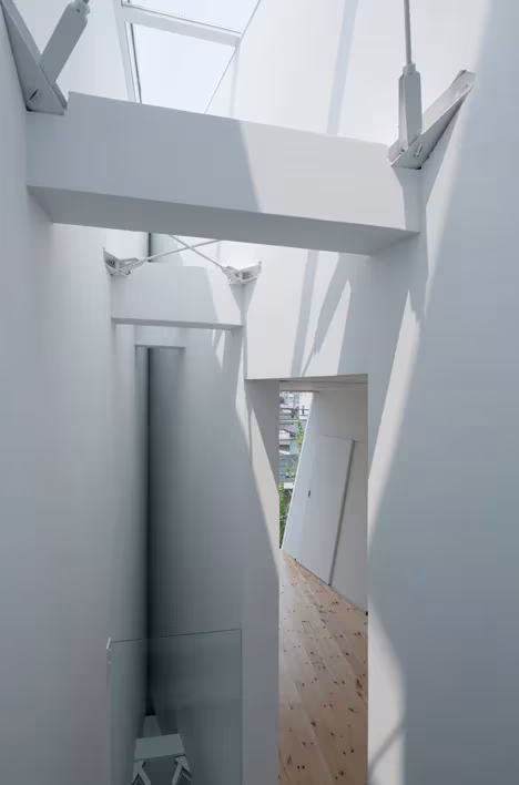 Hueco de escalera con lucernario y vigas atirantadas en el interior blanco de la Casa Tamatsu