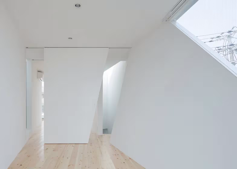 Estancia blanca de la Casa Tamatsu con muros oblicuos, suelo de madera y ventana inclinada