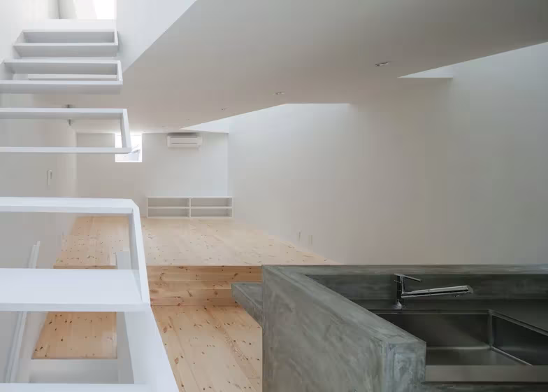 Cocina de hormigón con fregadero de acero bajo la escalera blanca en la Casa Tamatsu