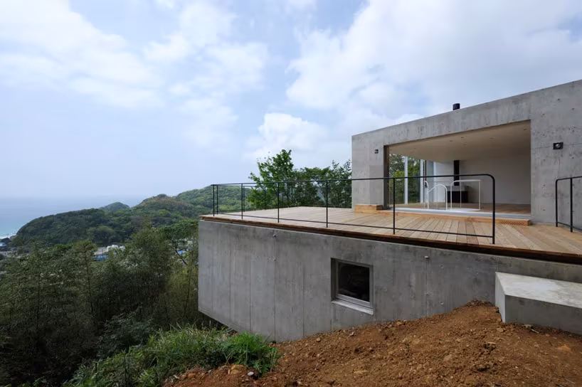 Volumen de hormigón de A House con terraza de madera asomada al mar desde la ladera