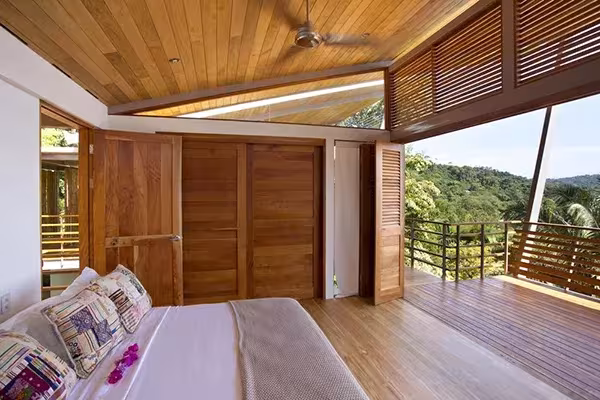 Dormitorio de la Casa Flotante con techo de madera, contraventanas de lamas y terraza abierta a las colinas