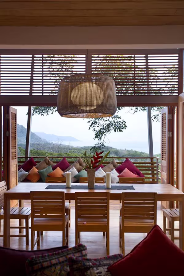 Comedor de la Casa Flotante con mesa de madera, lámpara de mimbre y vistas a la selva y la costa