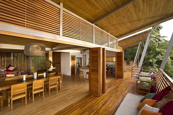 Espacio de día de la Casa Flotante con techo de madera, contraventanas abiertas y sofá junto a la barandilla