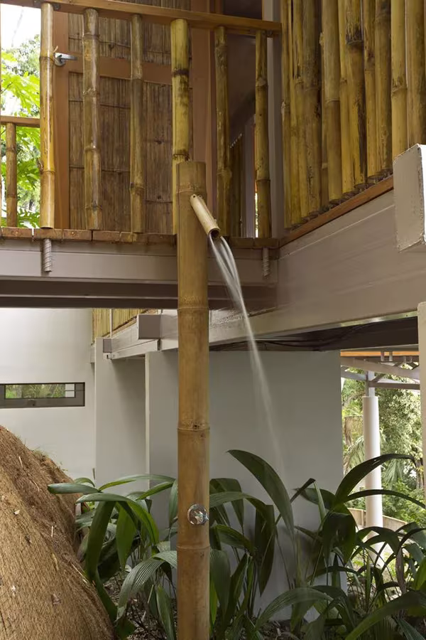 Ducha exterior de la Casa Flotante: un caño de bambú vierte agua entre rocas y plantas tropicales