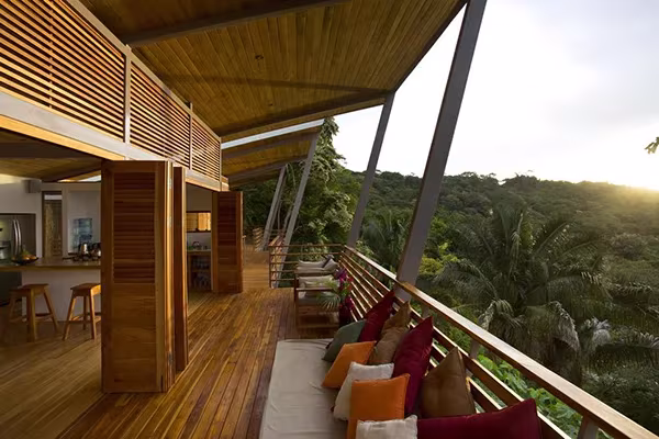 Terraza cubierta de la Casa Flotante al atardecer, con sofá de cojines de colores y lamas de madera