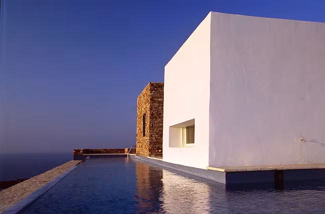 Volumen blanco de Kratir junto a una piscina desbordante que se funde con el mar al atardecer