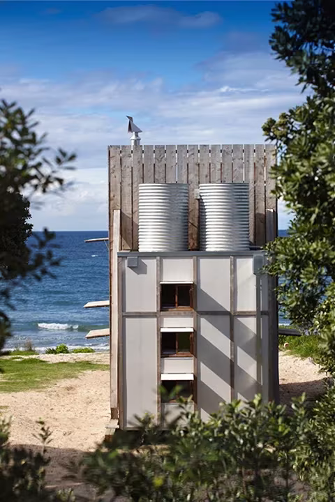 Cabaña de playa transportable de Crosson Clarke Carnachan cerrada, con depósitos de agua, junto al mar