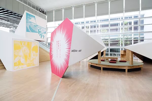Sala del YCAM con paneles inclinados rosa y blanco y gradas de madera circulares sobre suelo de parqué