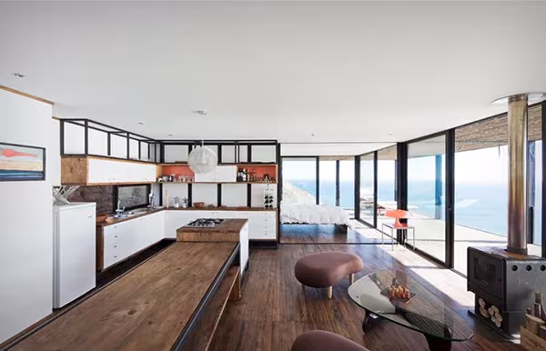 Salón cocina de la Casa Till con suelo de madera y grandes ventanales al Pacífico chileno