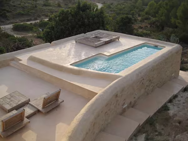 Piscina de la casa de Nani Marquina en Ibiza, de bordes curvos y muros terrosos, entre pinos y monte