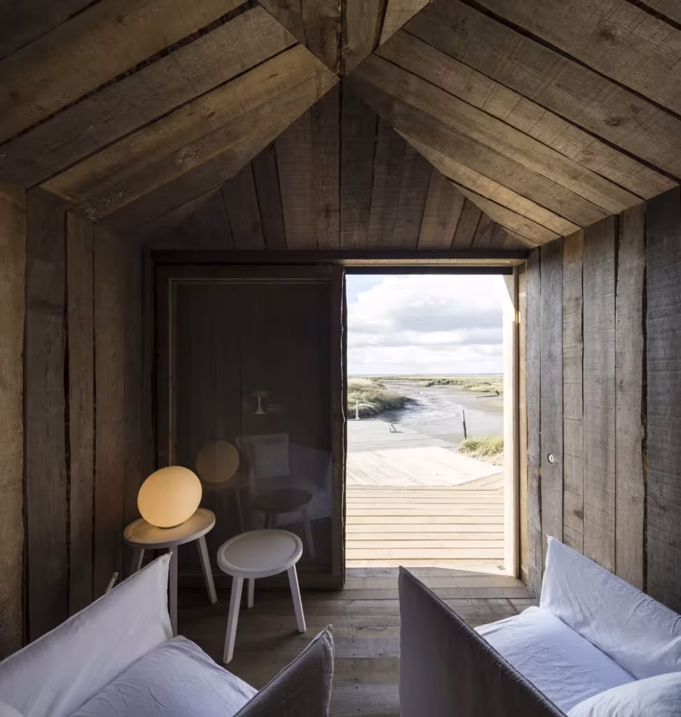 Interior a dos aguas de madera reciclada con sofás blancos y puerta abierta a la marisma de Comporta