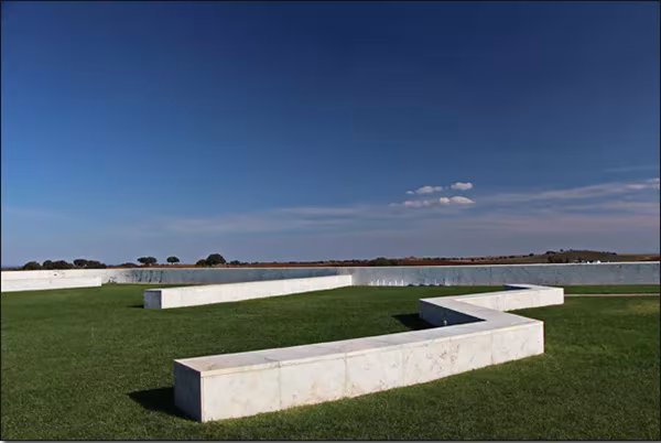 Banco de piedra en zigzag sobre el césped de la terraza de catas de la Adega Maior, bajo el cielo azul