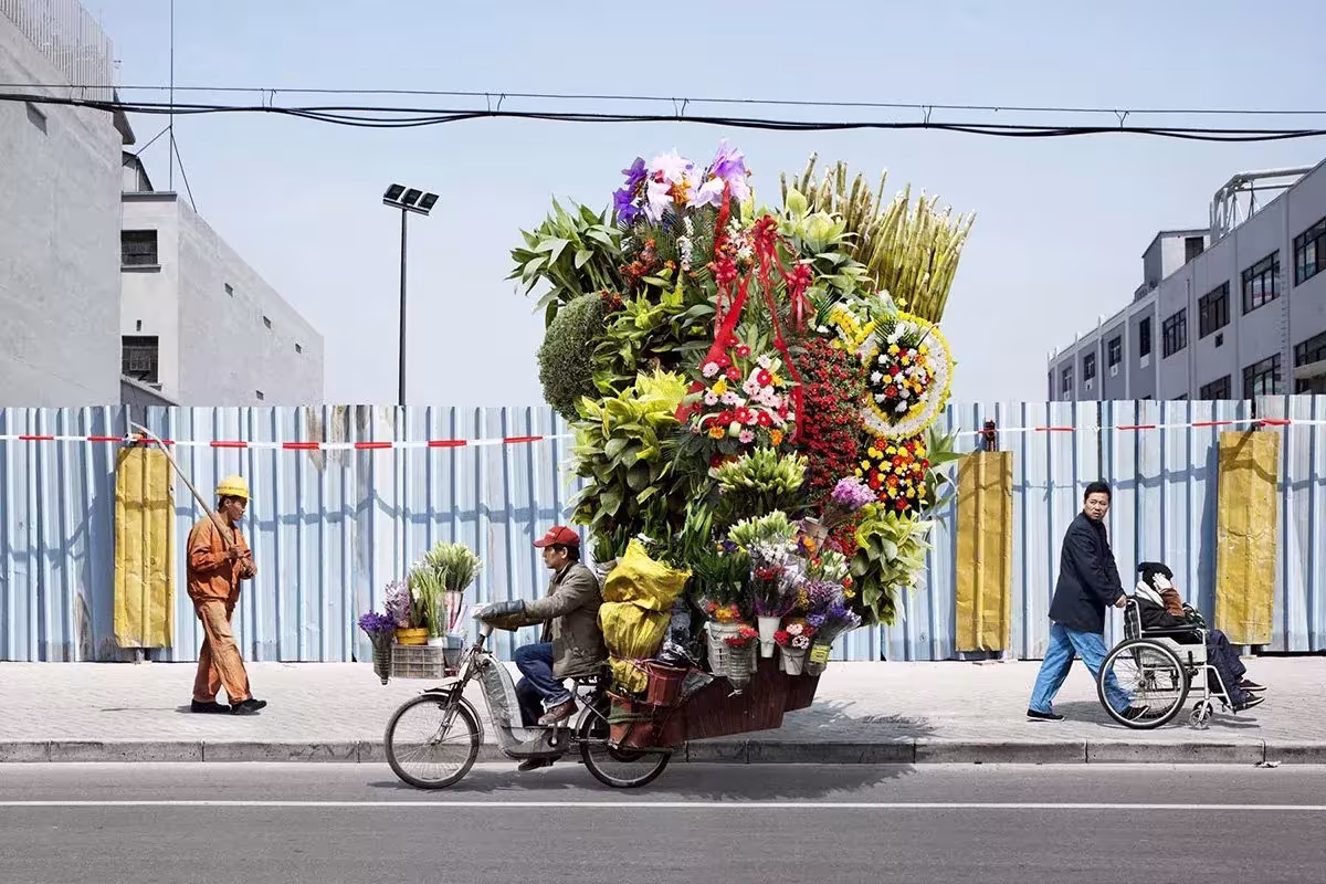 Bicicleta cargada con una enorme torre de flores en una calle asiática, serie Tótems de Alain Delorme