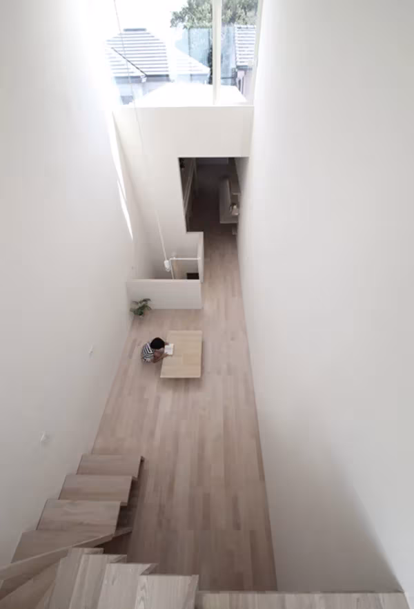 Vista cenital del estrecho interior de la Imai House con escalera de madera y suelo claro