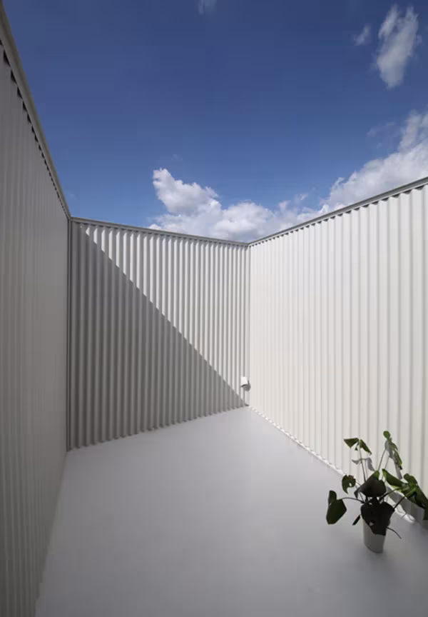 Patio abierto al cielo de la Imai House entre paredes de chapa ondulada blanca, con una planta