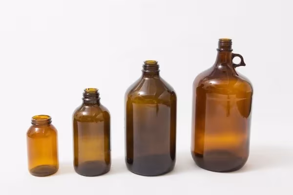 Cuatro botellas de vidrio ámbar de distintos tamaños, la materia prima reciclada de las lámparas Utrem Lux