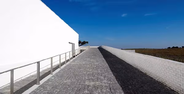 Rampa adoquinada junto al muro blanco de la bodega Adega Maior de Álvaro Siza bajo un cielo azul