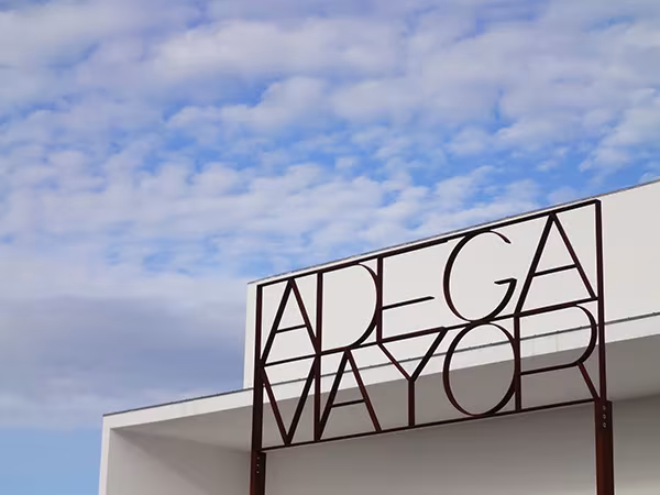 Letras metálicas de la bodega Adega Mayor sobre el edificio blanco de Álvaro Siza ante un cielo nublado