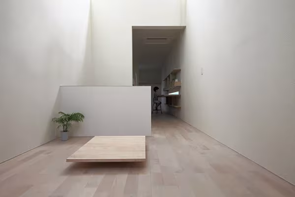 Estancia blanca de techos altos con tarima baja de madera y planta en la Imai House