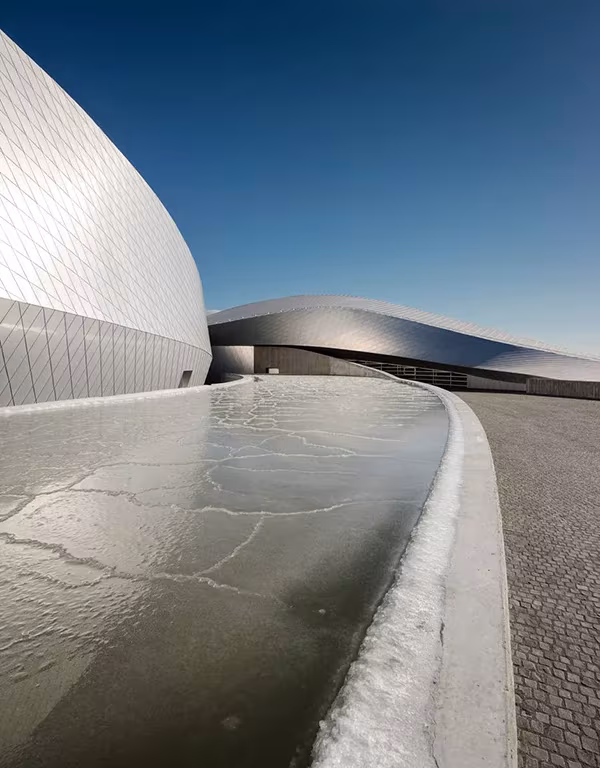 Fachada curva de escamas de aluminio del acuario El Planeta Azul junto a un canal de agua helada