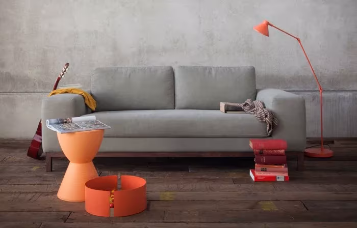 Sofá gris de Ethnicraft con lámpara de pie y mesitas naranjas sobre suelo de madera oscura