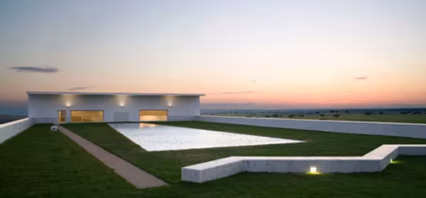 Adega Maior de Álvaro Siza al anochecer, con la terraza de césped, lámina de agua y bancos iluminados