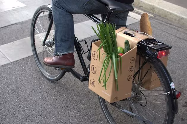 Alforja Packtasche de cartón con puerros y pan colgada del portaequipajes de una bicicleta
