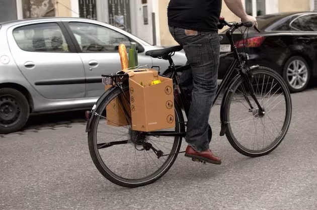 Bicicleta negra con alforjas de cartón Packtasche junto a coches aparcados en la calle
