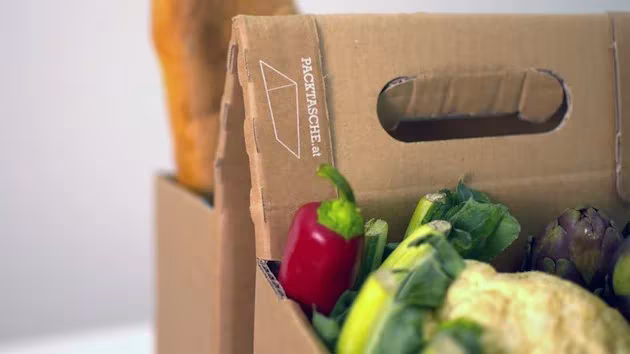 Detalle de una alforja de cartón Packtasche con asa troquelada llena de pimientos y verduras