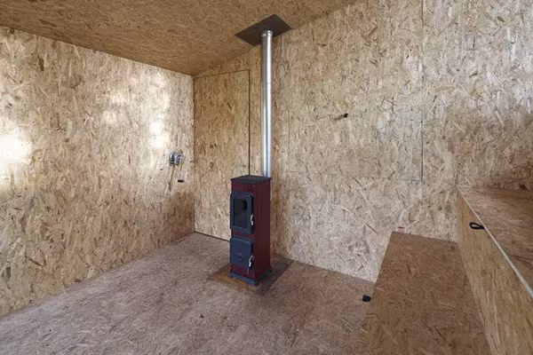 Interior de tablero OSB con estufa de leña y banco corrido en la cabaña de Uhlik Architekti