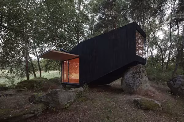 Cabaña mirador de madera negra en voladizo sobre una roca en un claro del bosque de Bohemia