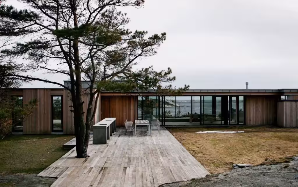 Cabaña Jesper de Lund Hagem con fachada de cedro y terraza de tablones entre pinos junto al mar noruego